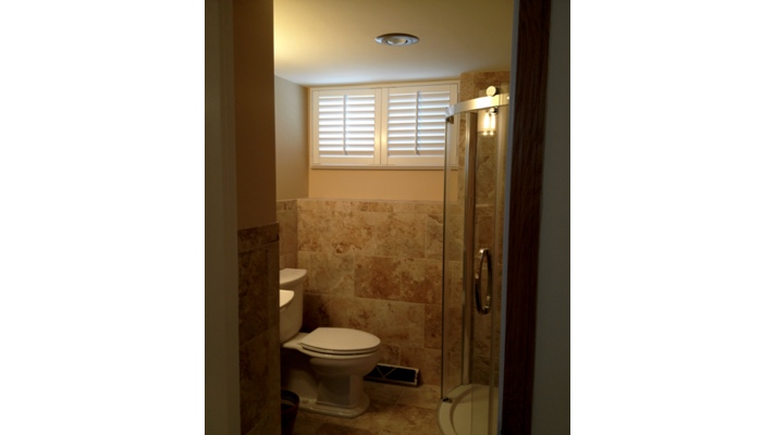 Small basement bathroom window covered in white plantation shutters